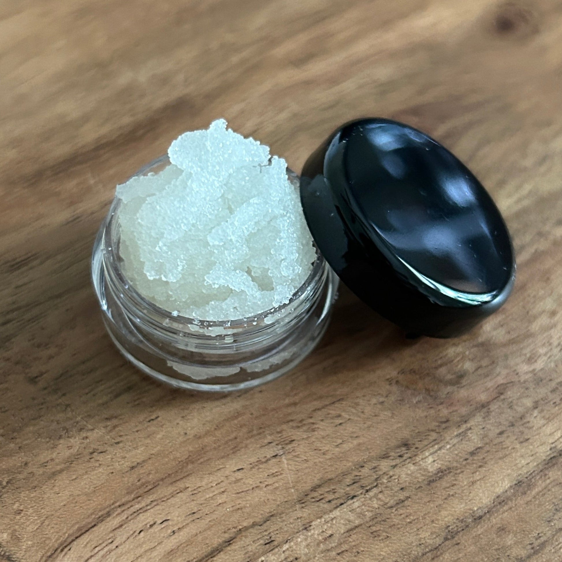 Small container with body scrub on a wooden surface